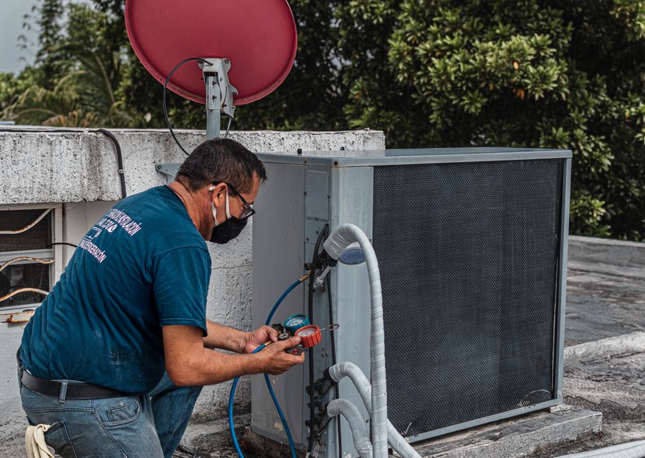 HVAC technician repairing an outdoor air conditioner unit with manifold gauges